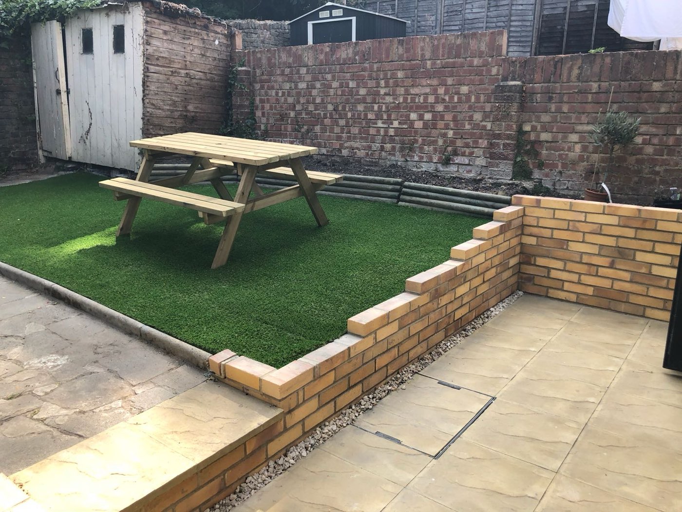 Rear garden with a brick retaining wall, lawn and paving at Tourmount Road, by LINX
