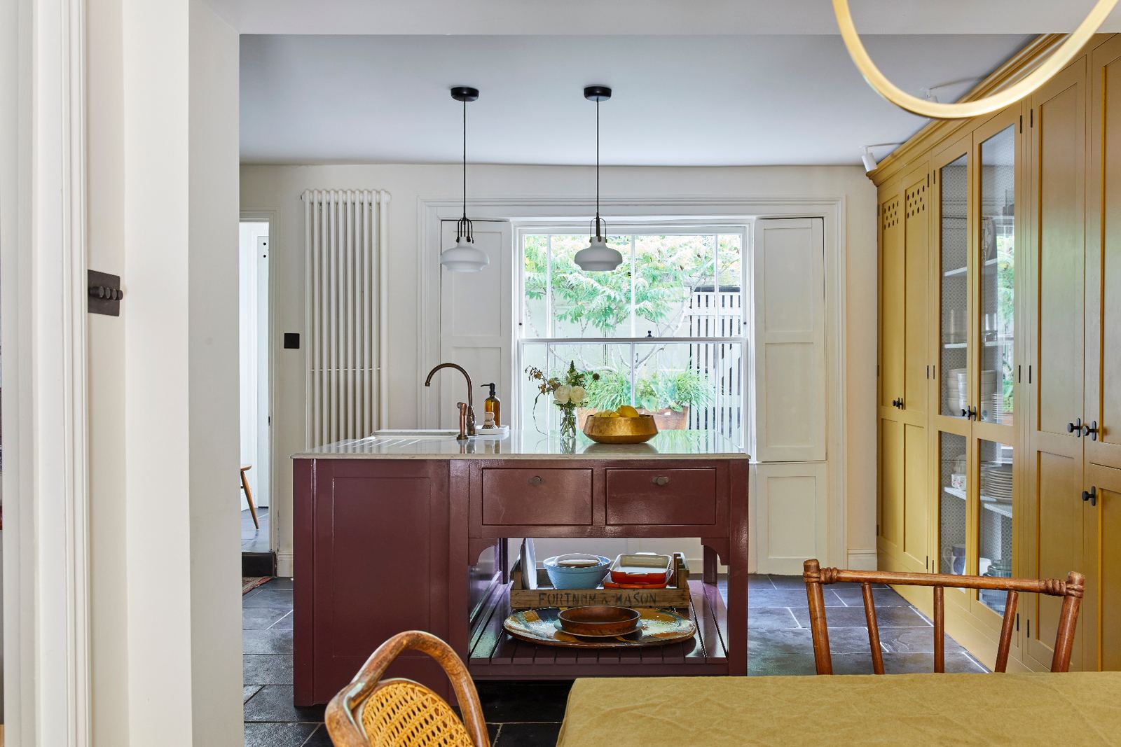 Kitchen with a burgundy island, brass pendant lights and tall glazed cabinets in a period home renovated by LINX