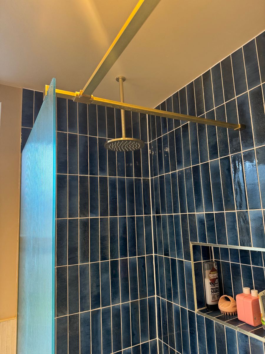 Walk-in shower lined with deep blue glazed tiles and brushed brass fittings in a LINX project
